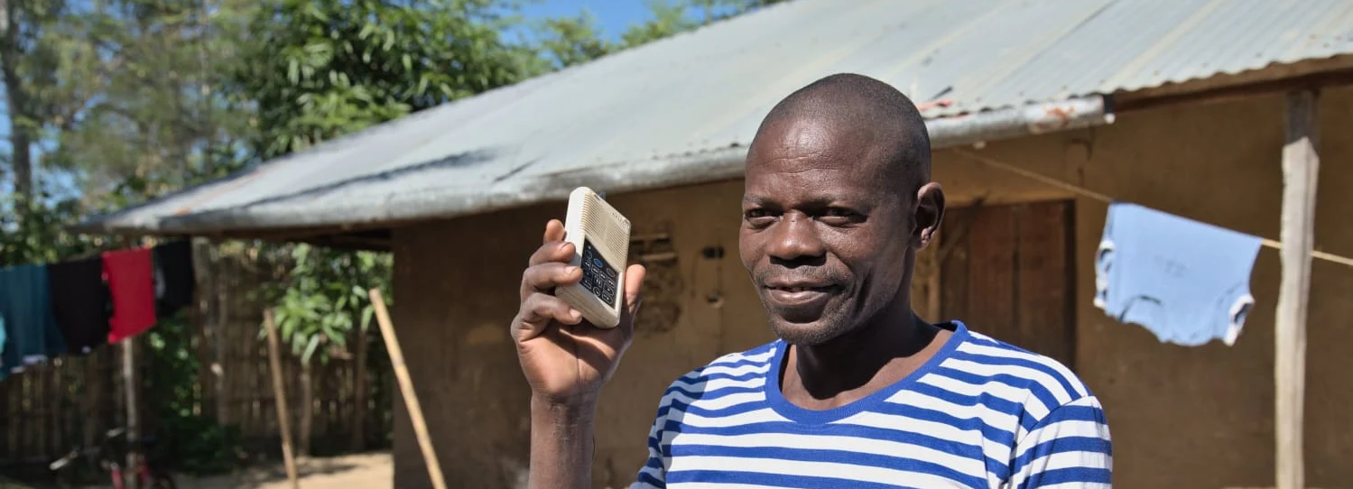 A smiling man holding a small audio device up to his ear in Mozambique.