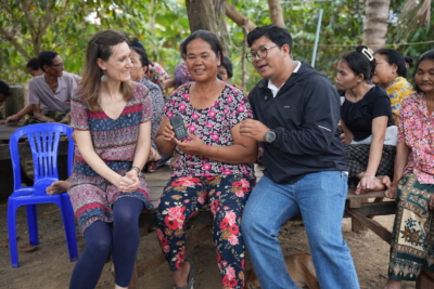 Feba staff member, Ruth, sits catting on a wooden platform with a female listener and Kiry, a member of the Khmer Audio Bible team in Cambodia.