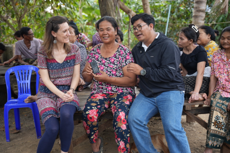 Feba staff member, Ruth, sits catting on a wooden platform with a female listener and Kiry, a member of the Khmer Audio Bible team in Cambodia.