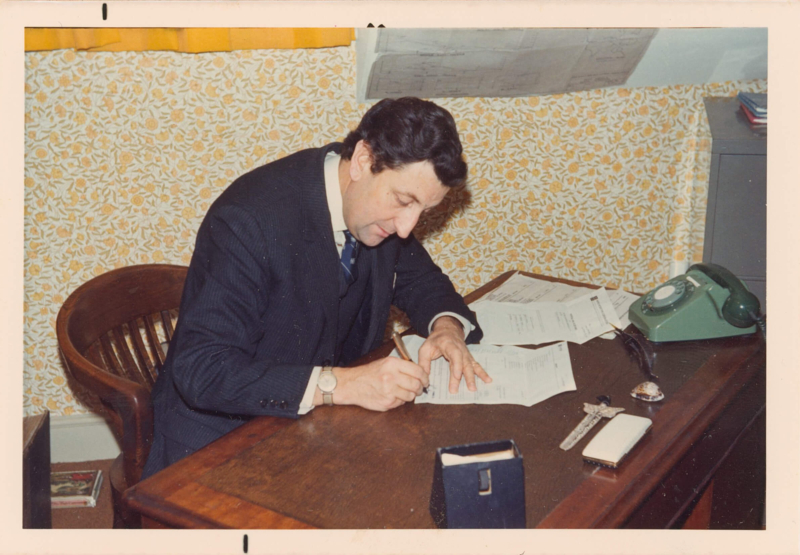 Douglas Malton, Feba founder, sits at a wooden desk writing. He has dark brown hair and is wearing a navy suit.