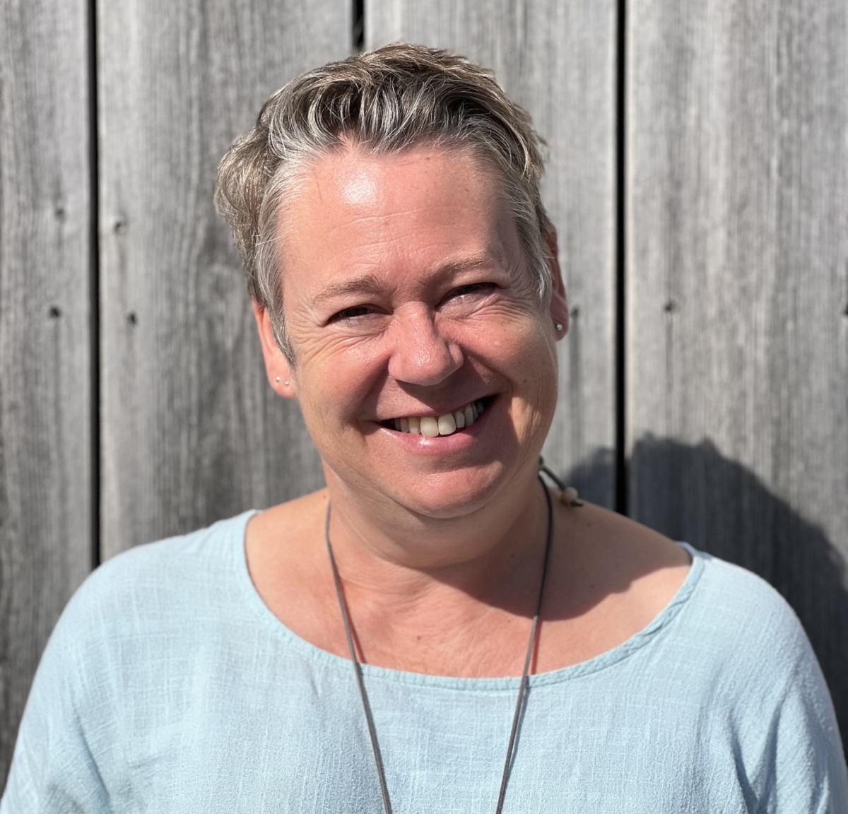 Esther smiling, wearing a light blue top. She has short grey hair.