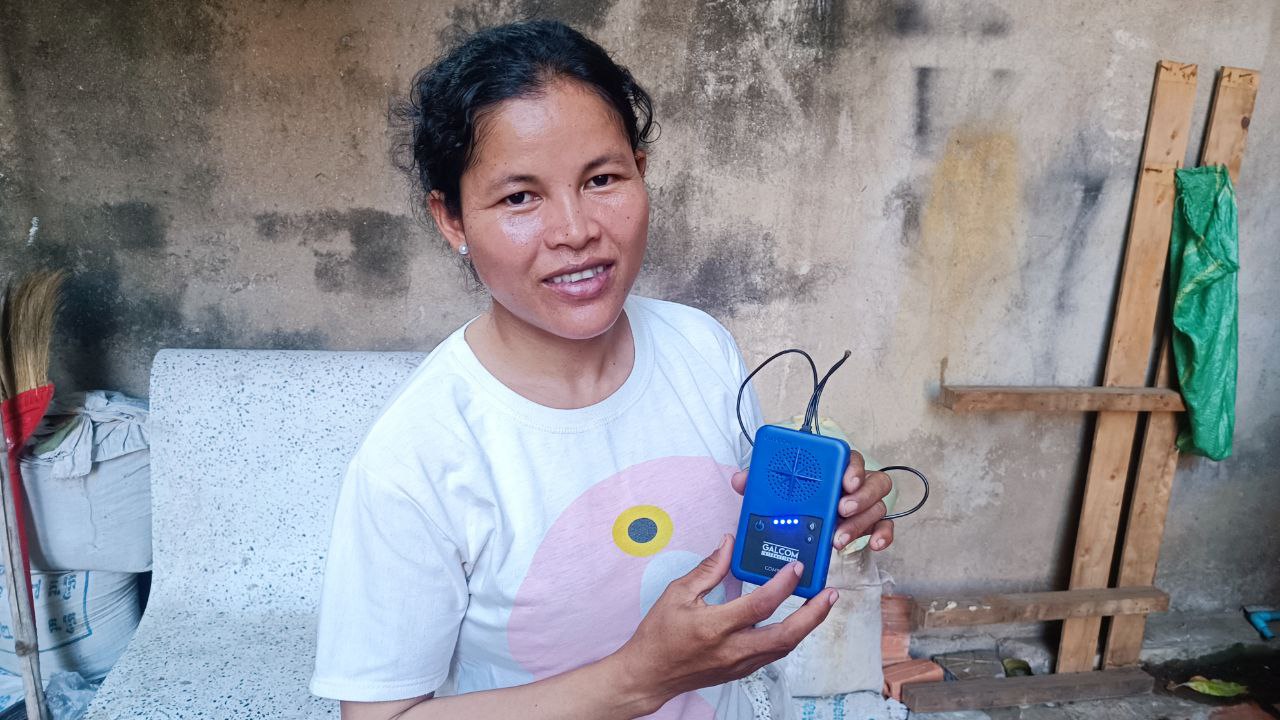 A female listener in smiling and Cambodia holding a blue audio Bible.