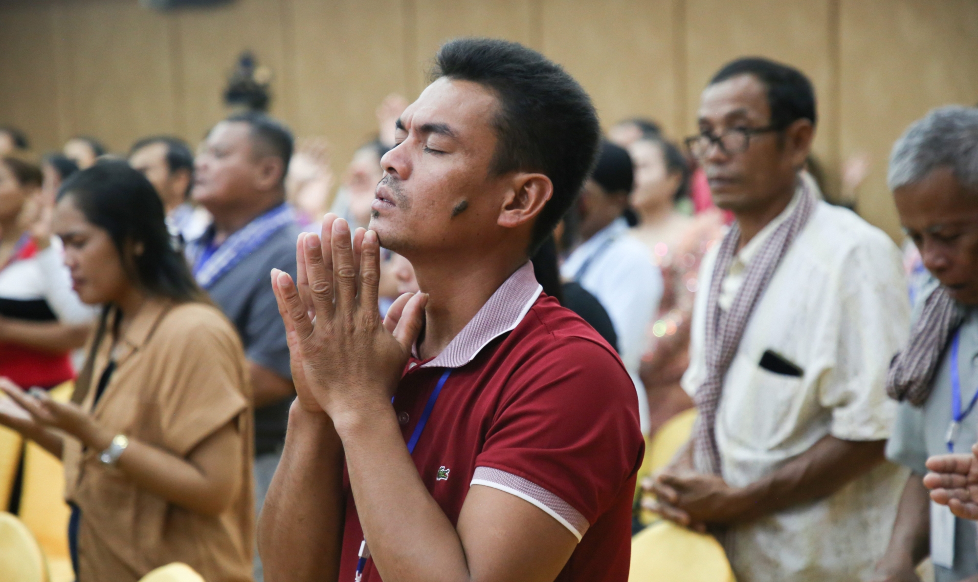 A young man holds his hands together in prayer and worship at a conference in Cambodia.