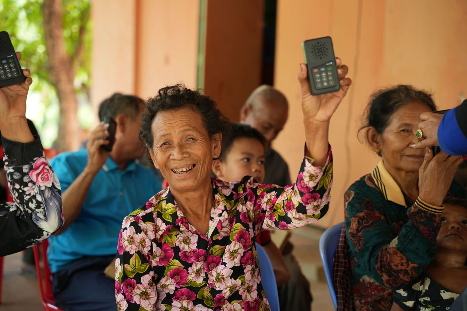 An older woman grinning as she holds an audio Bible above her head in Cambodia. She is surrounded by other people also holding audio Bibles.