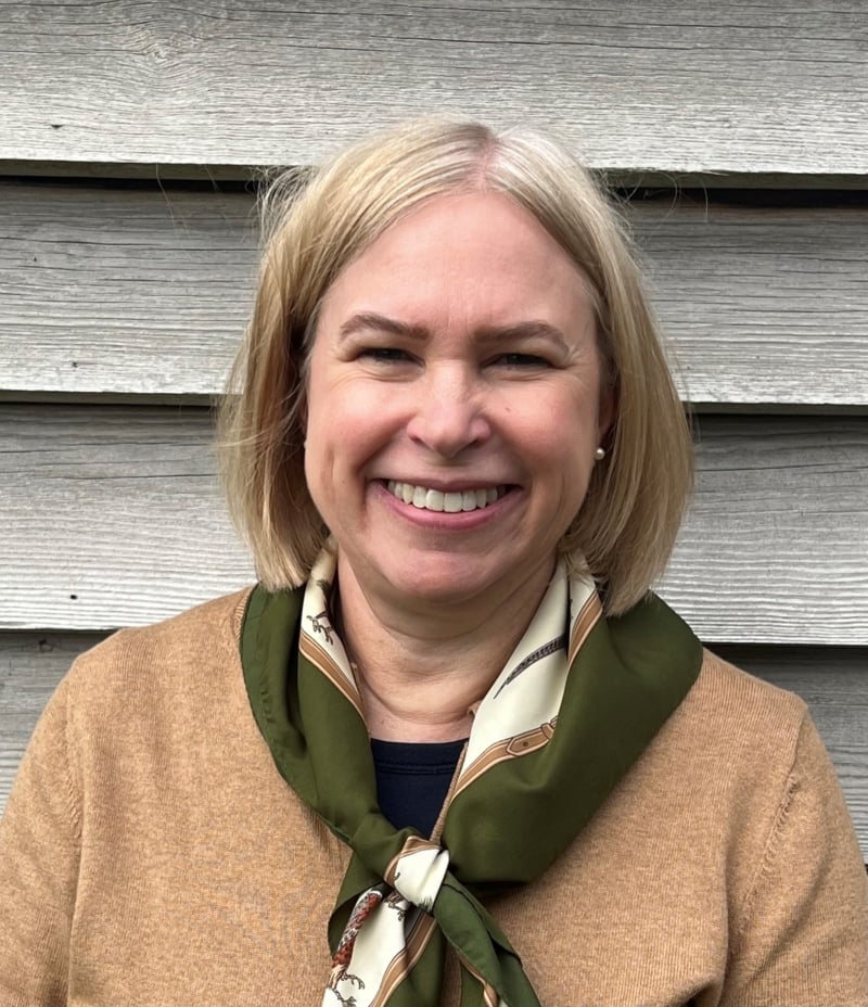 Sarah smiling. She has a blonde bob and is wearing a beige jumper with a green and white neck scarf.