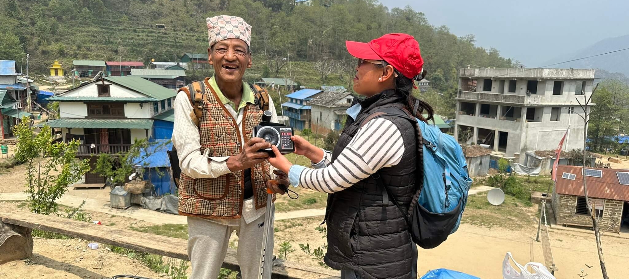 Binu, a staff member at Afno FM in Nepal, handing a radio to an older Nepali man who is grinning at the camera.