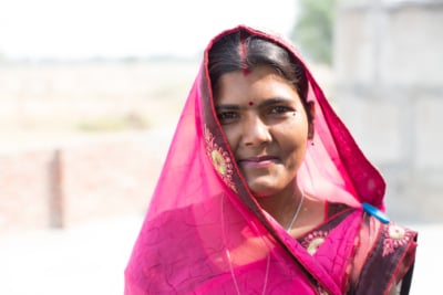 A portrait of a smiling young Indian woman wearing a beautiful pink sari.