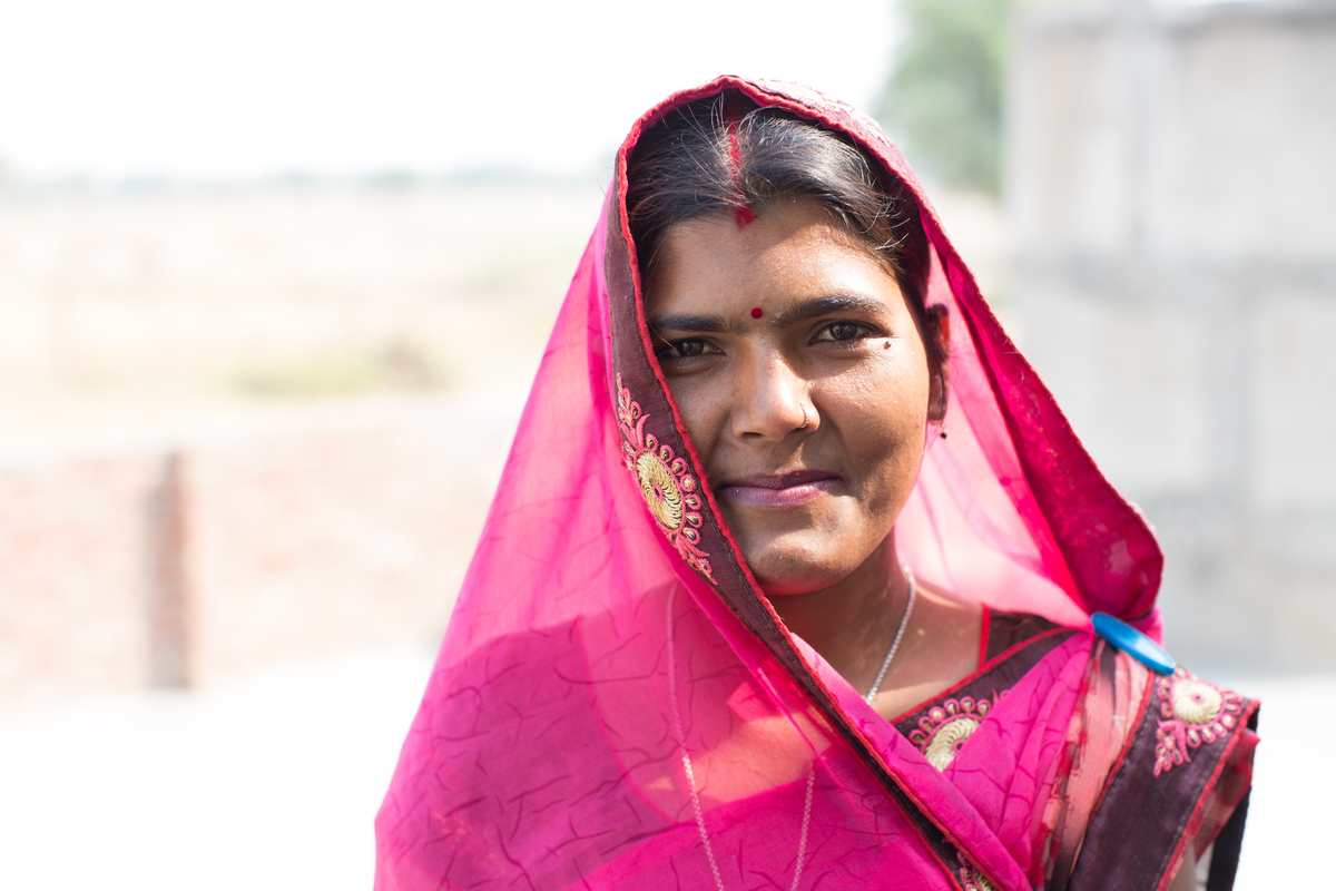 A portrait of a smiling young Indian woman wearing a beautiful pink sari.
