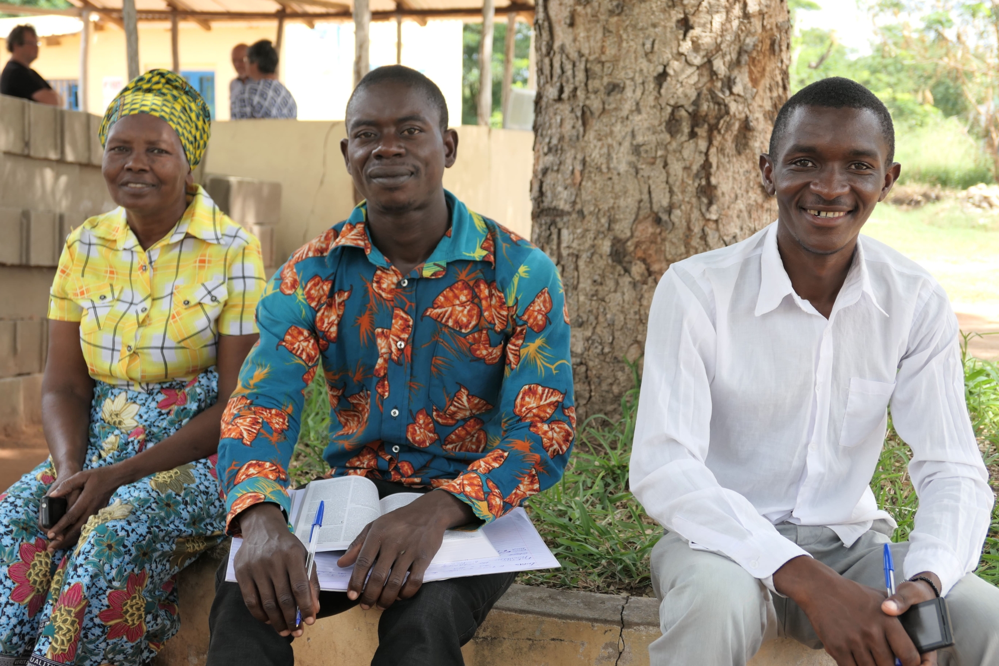 Two men and a lady sit on a small wall smiling during a Bible study in Mozambique.