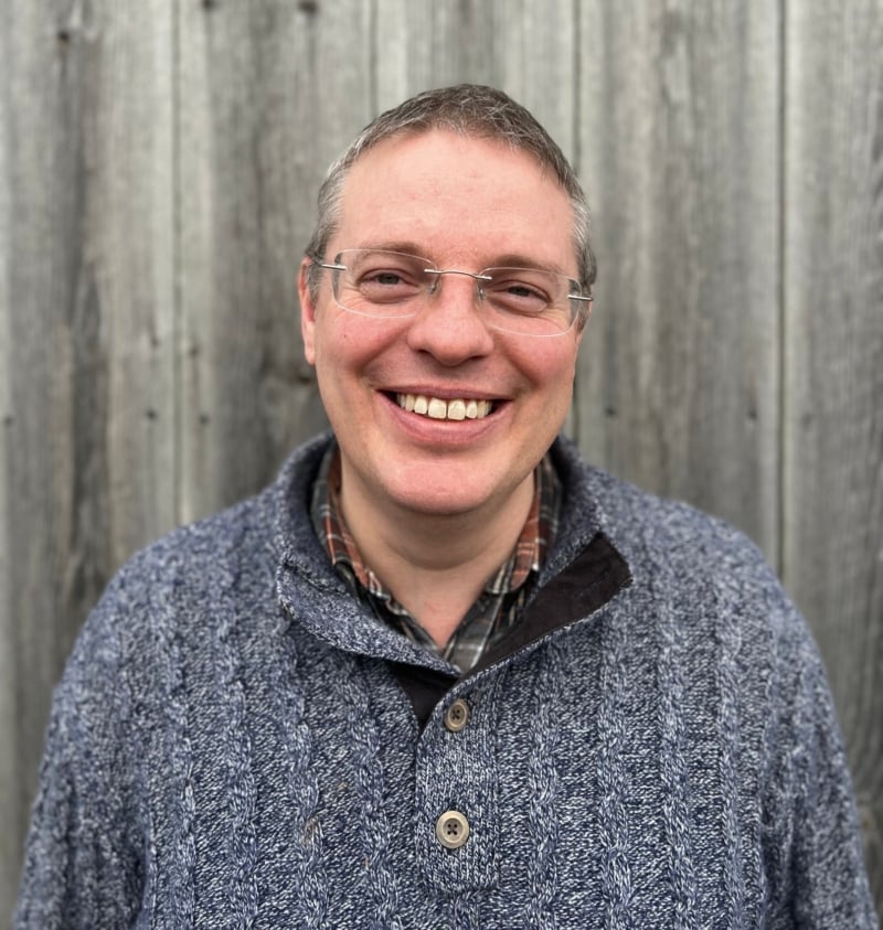 A smiling headshot of Neil, Feba's Head of International Ministry. He has short grey hair, clear rimmed glasses and is wearing a blue knit jumper.