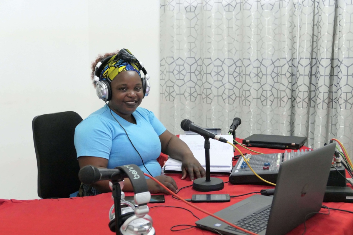A young woman recording a radio broadcast at the Radio Wimbe Studio in Mozambique, smiling at the camera.