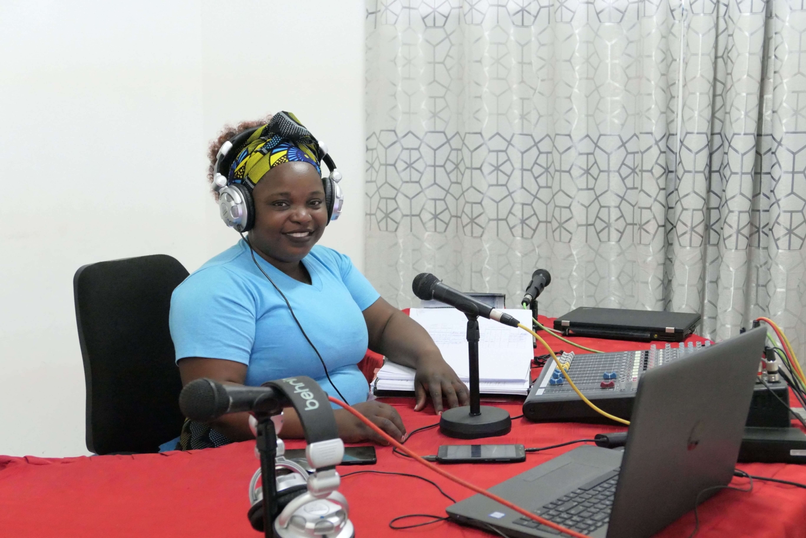 A young woman recording a radio broadcast at the Radio Wimbe Studio in Mozambique, smiling at the camera.