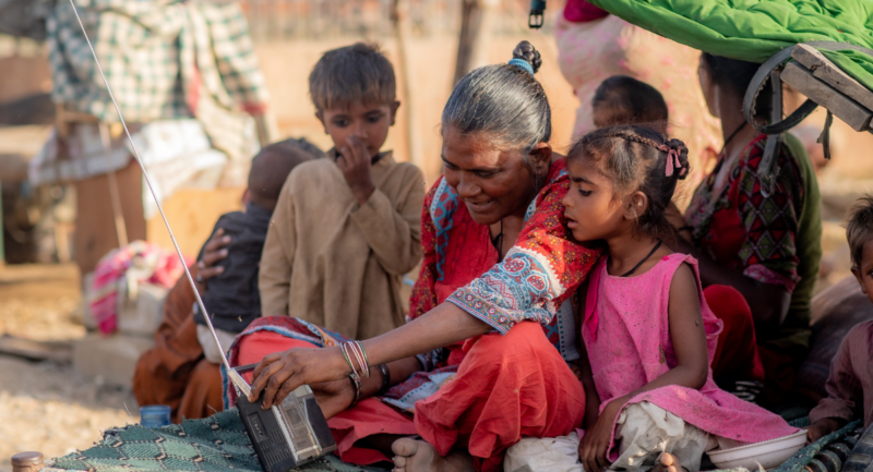 A mother with her two young children sit on a day bed in Pakistan, listening to a radio.