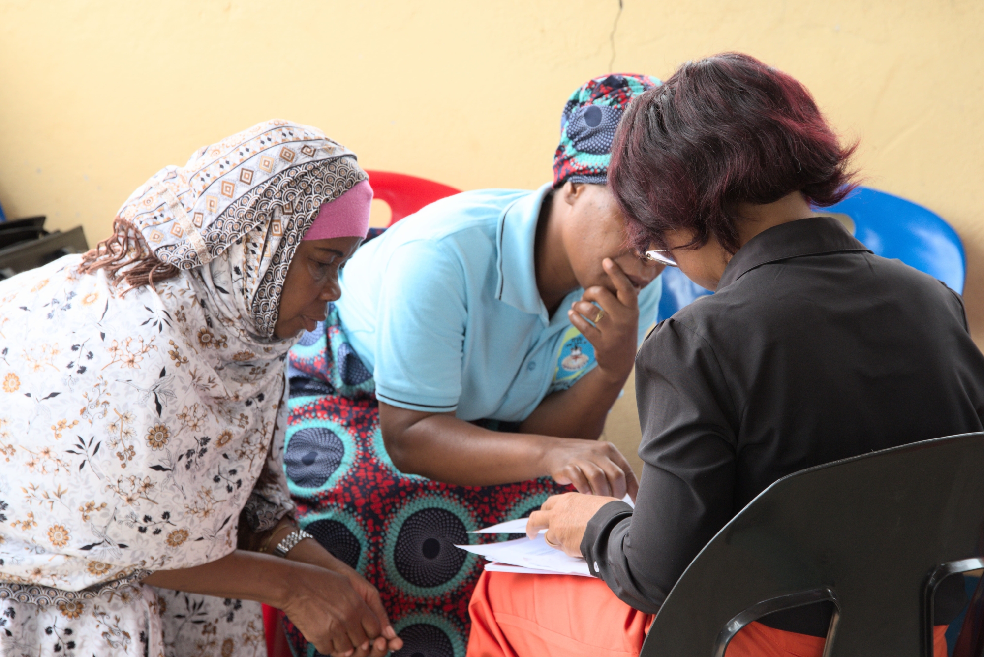 Three women from the Radio Wimbe staff team sitting together leaning over and discussing a document.
