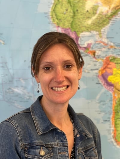 Ruth smiling at the camera, with a map of the world in the background.