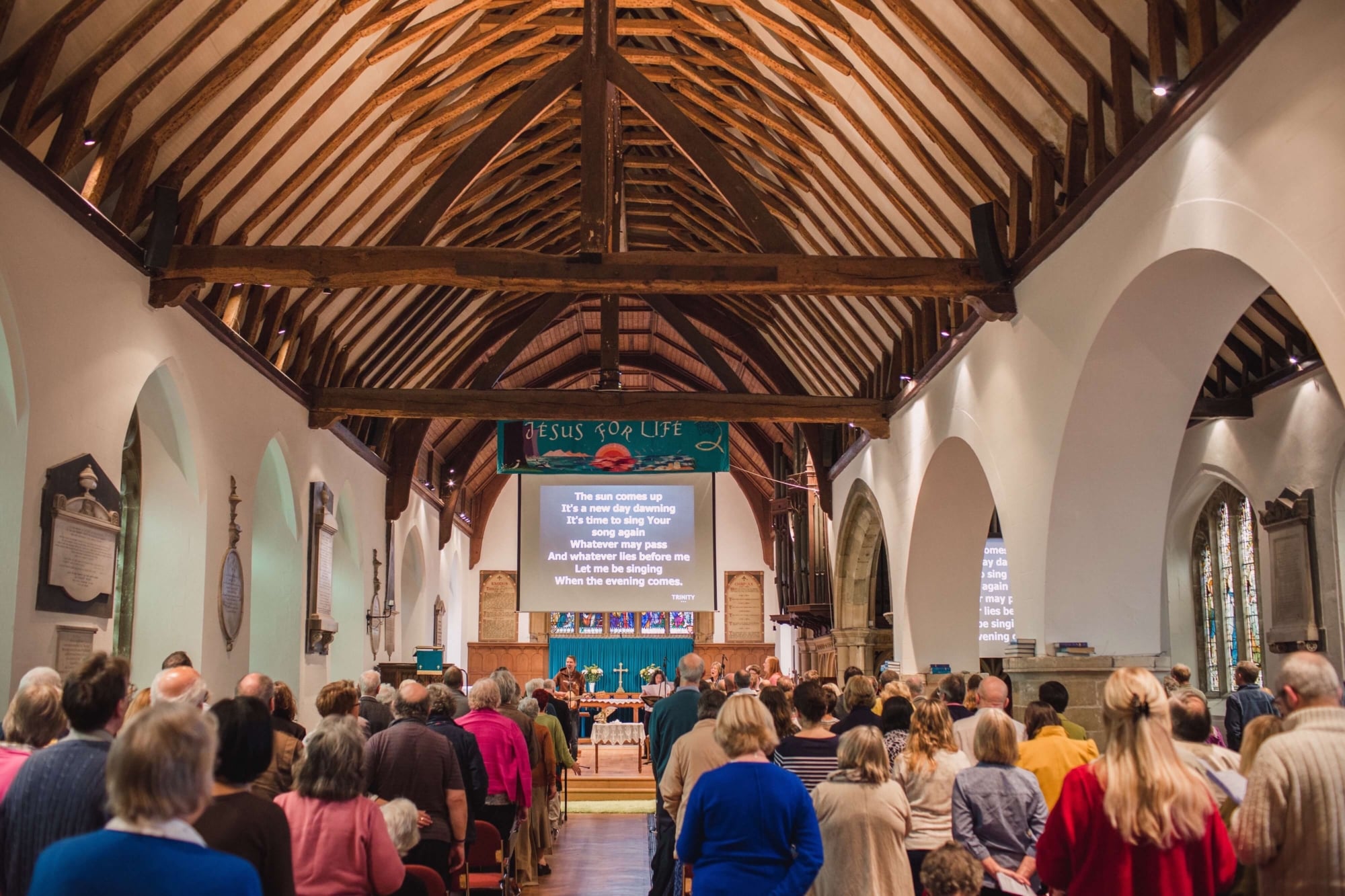 A UK congregation standing in a traditional wooden beamed church, singing worship songs.