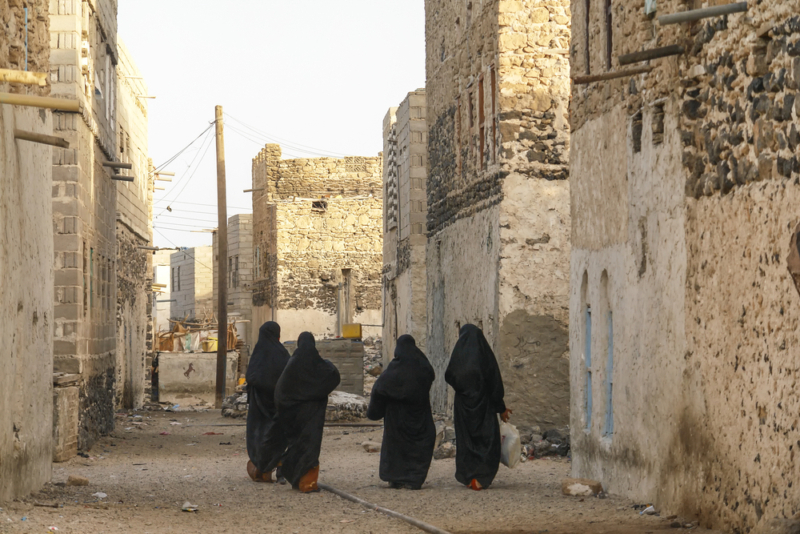 Women walking along a street in Yemen, with their backs to the camera, wearing all black outfits and hijabs.