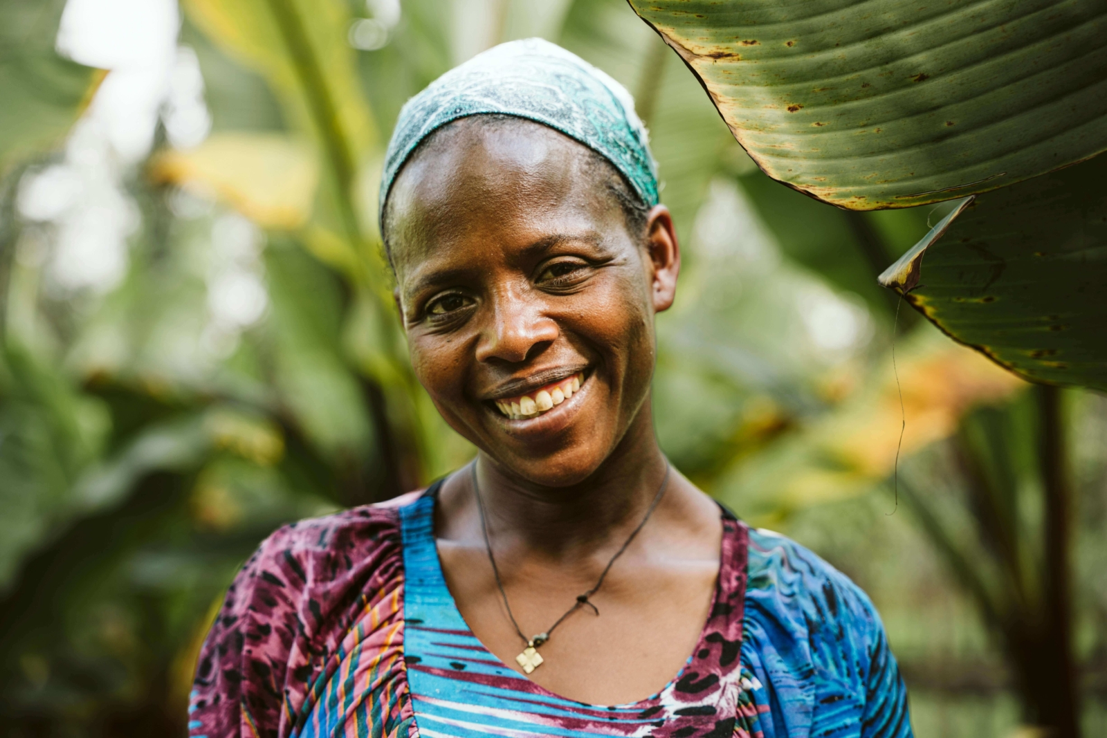 Portrait of a woman in a colourful dress and headscarf smiling in Ethiopia, surrounded by green palm leaves.