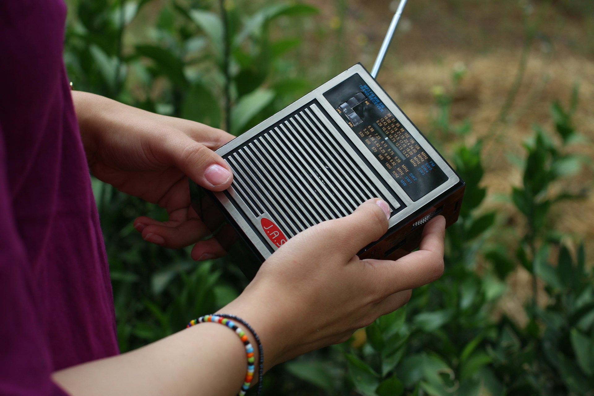 A close up of hands holding a small old fashioned square radio with an ariel and tuning dial.