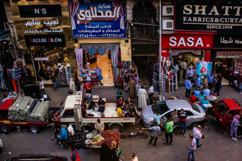 A busy street in Egypt with cars, people walking and rows of shops selling fabric.