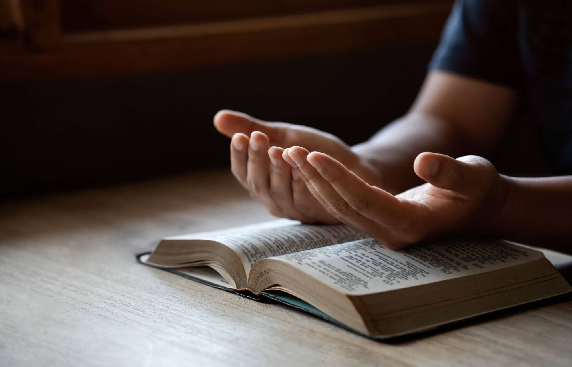 Close up of hands open in prayer, resting on a Bible.