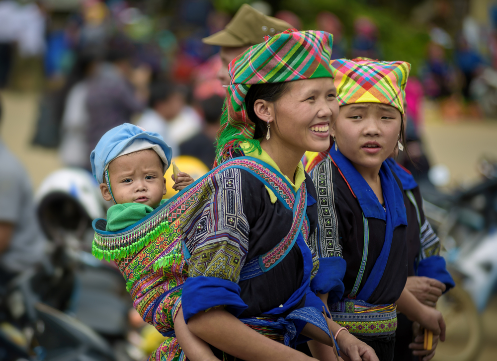Two young Vietnamese woman in traditional dress. One has a young baby on her back.