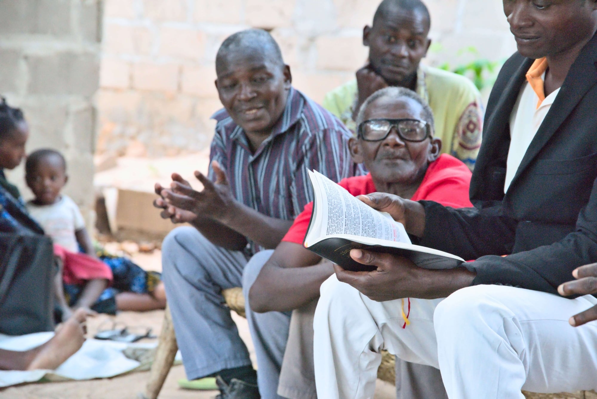 A group of men in Mozambique gathered around a Bible having a discussion.