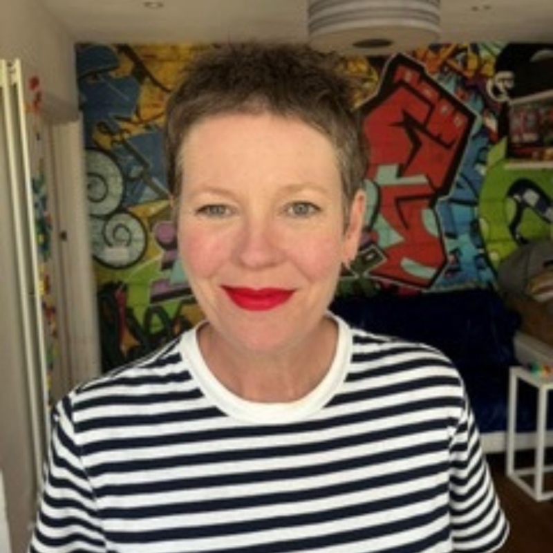 A headshot of Aly, Feba's bookkeeper. She has a pixie cut, bright red lipstick and is wearing a black and white striped tshirt.
