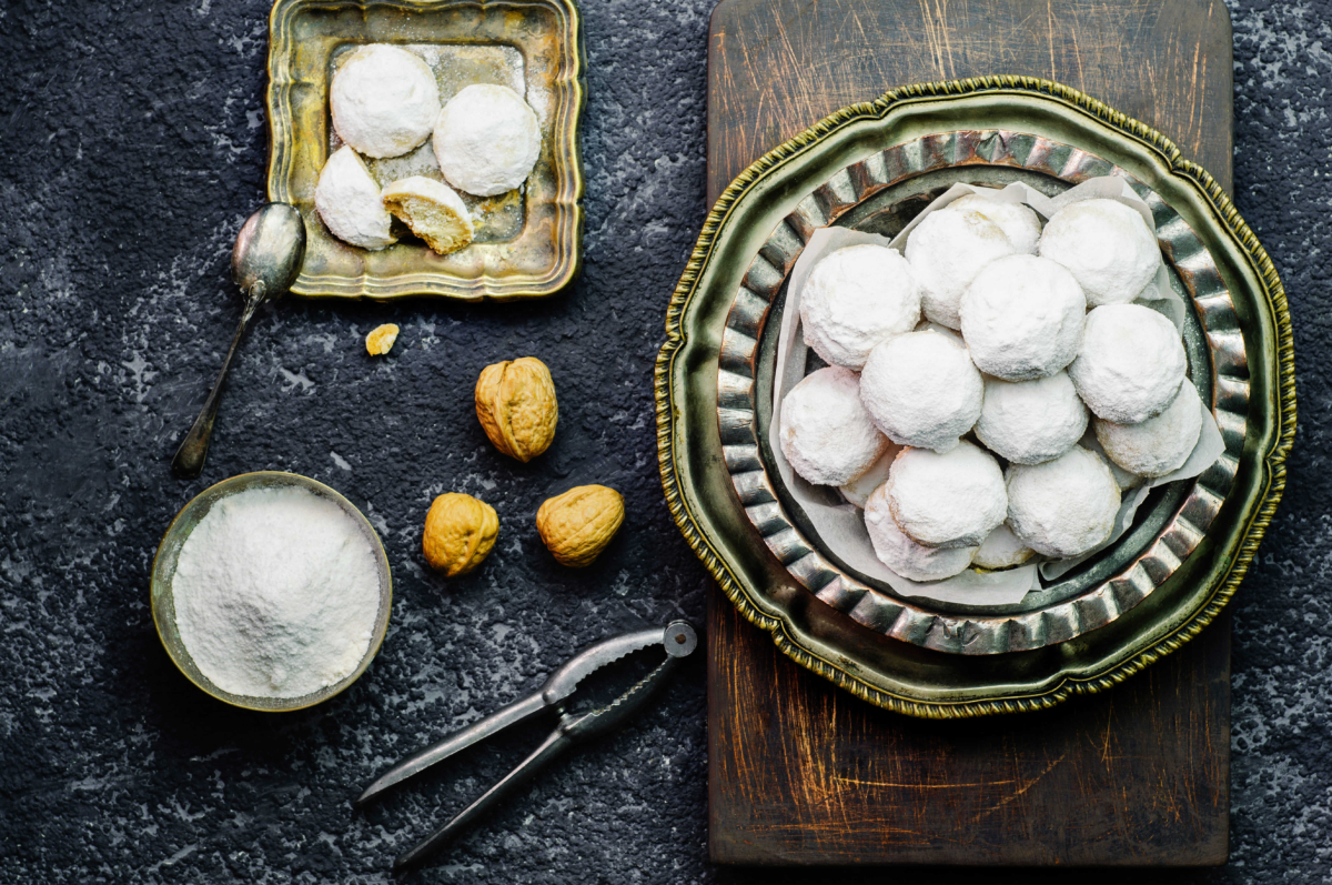 Overhead shot of a table with a bowl of small Kahk cookies covered in powdered white sugar.