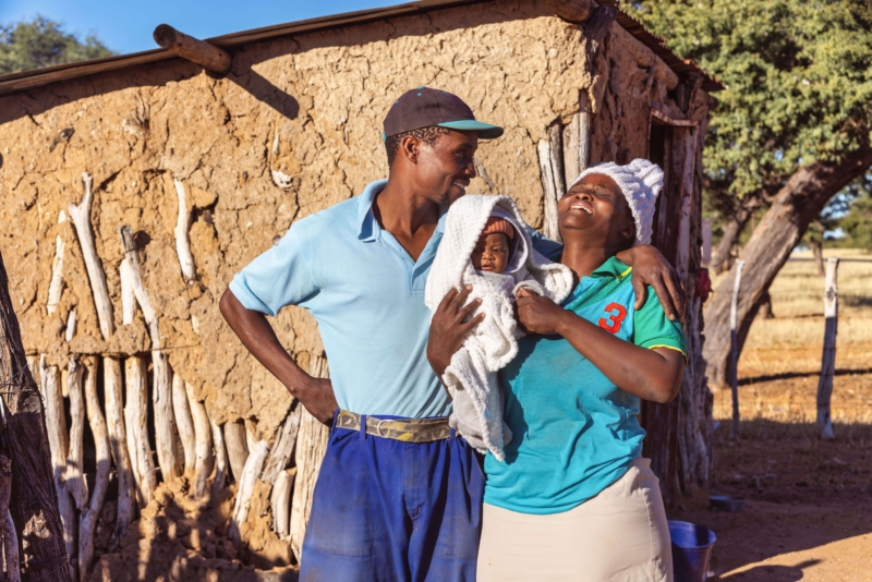 A husband and wife holding a small baby laughing in a rural village in Ethiopia.