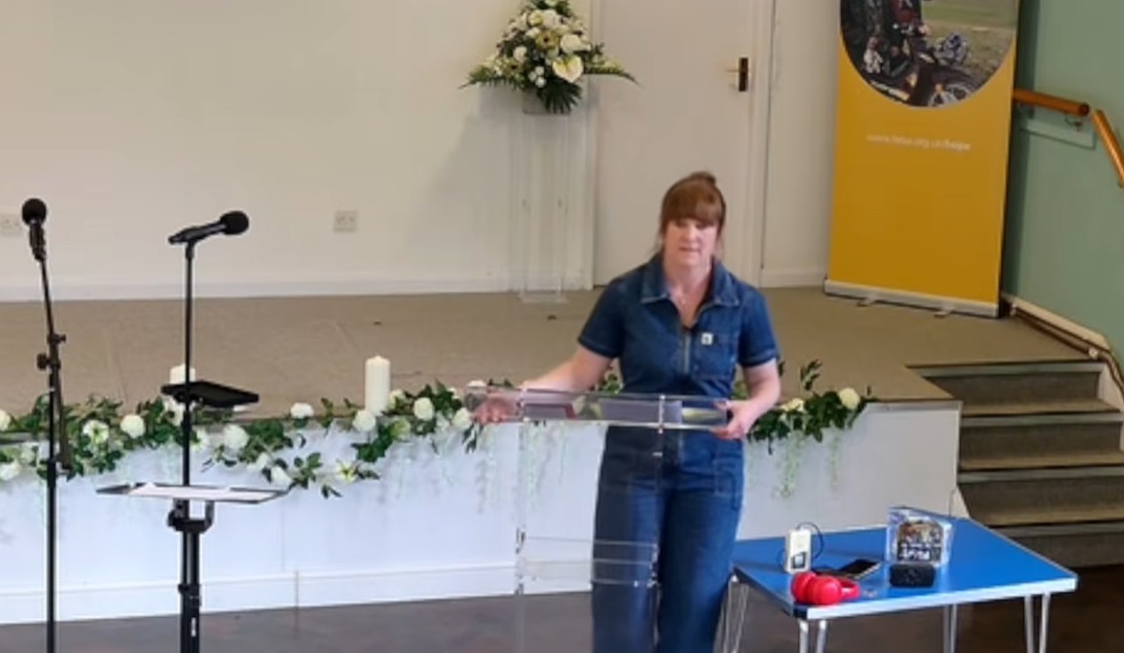 Emily stands at a lectern in a church hall giving a presentation about Feba.
