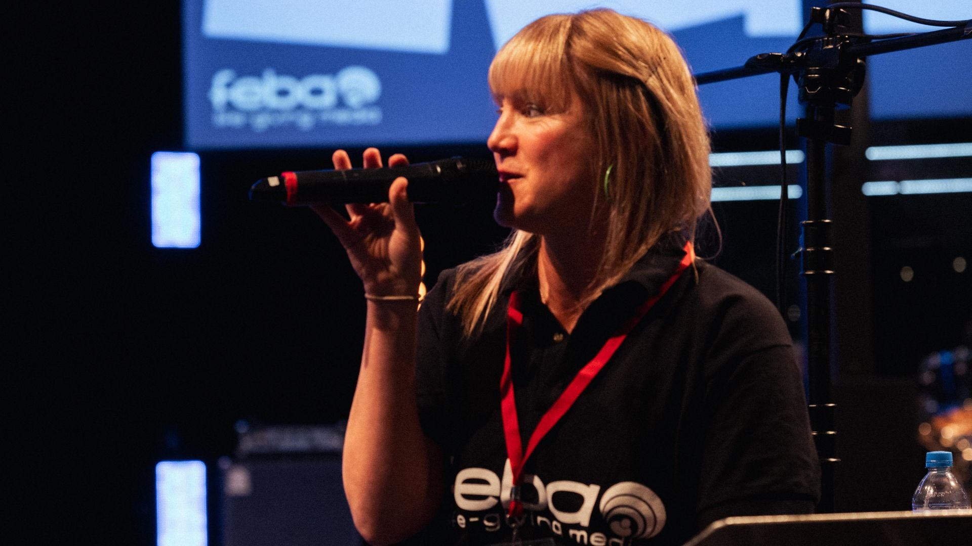 Feba staff member, Emily, speaking into a microphone on stage at the Church Sound and Media Summit.