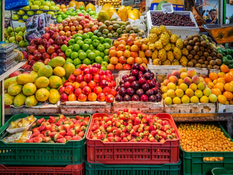 Market stall full of different colourful fruits including strawberries, apples, kiwis and melons.