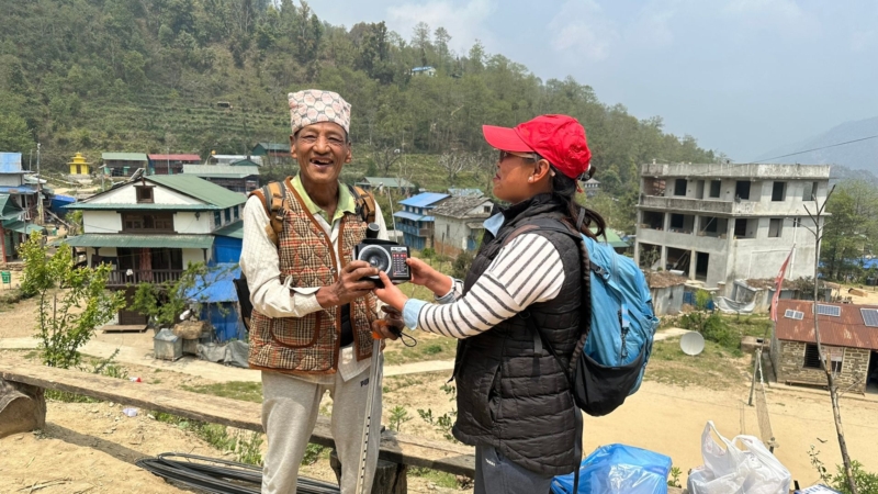 Binu, a staff member at Afno FM in Nepal, handing a radio to an older Nepali man who is grinning at the camera.