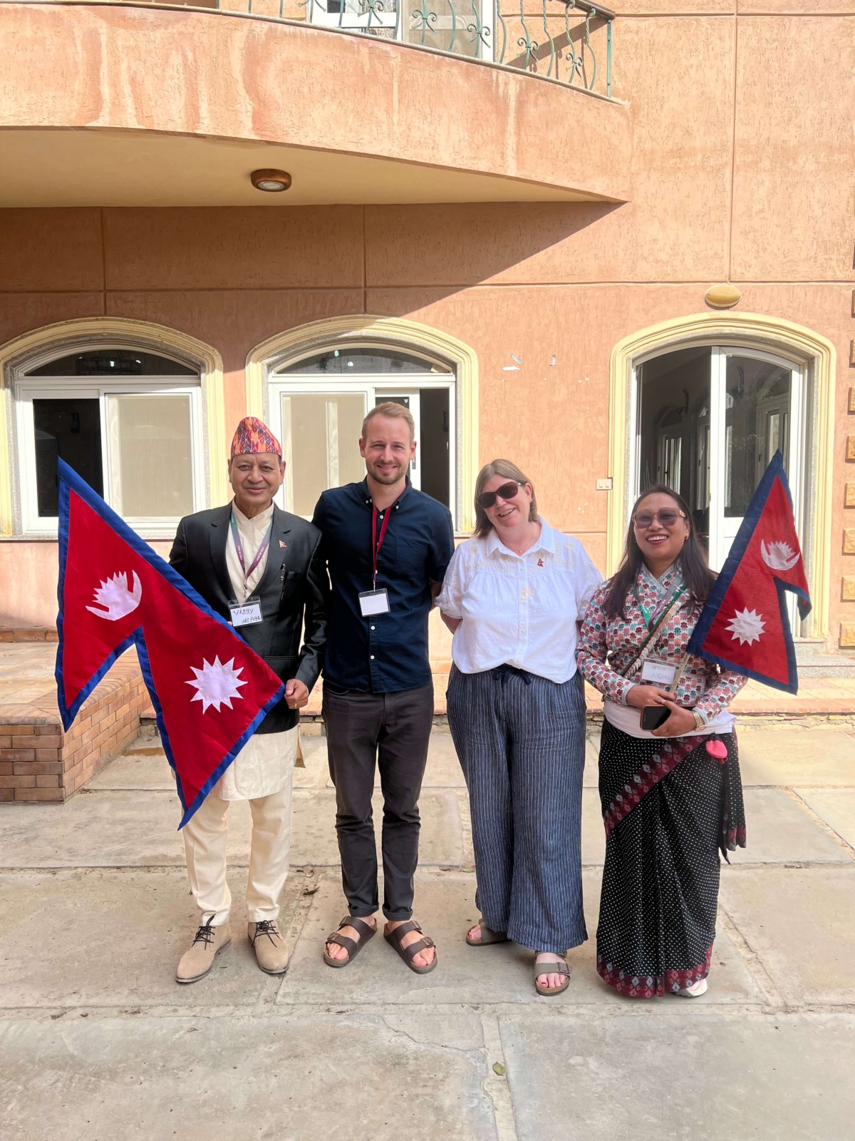Feba staff members Luke and Catherine stand with Nepalese partners Vijay and Binu who work for Afno FM. Vijay and Binu are both holding Nepal flags and wearing traditional Nepalese clothes.