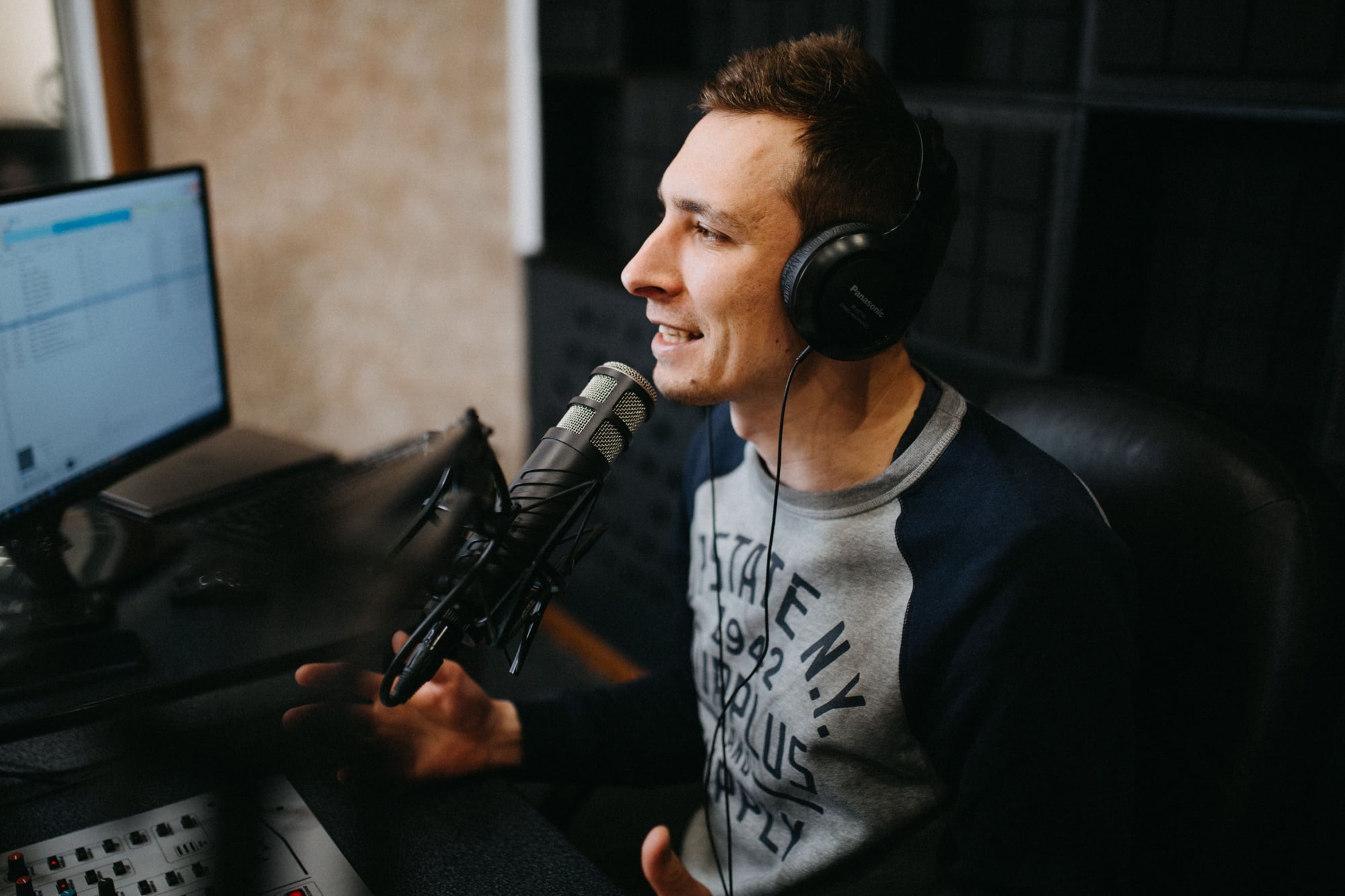 A young man sitting at a recording desk, wearing headphones and animatedly talking into a radio mic in Ukraine.
