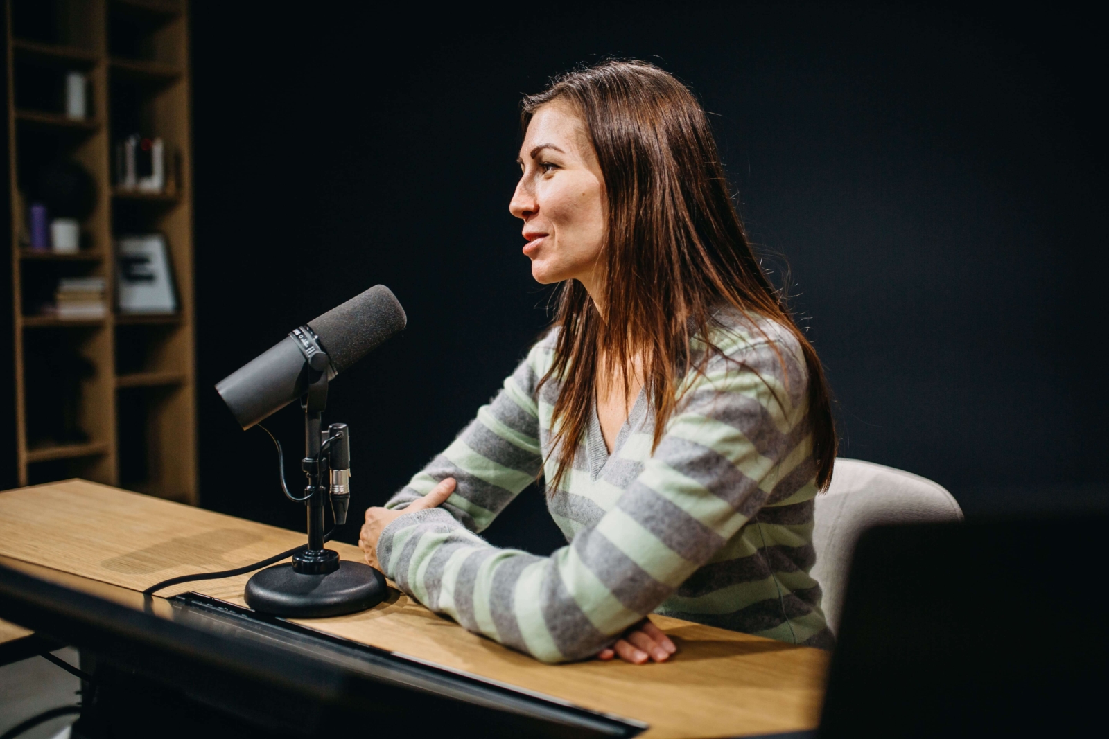 A young Ukrainian woman with straight, long brown hair sits at a desk talking into a radio mic.