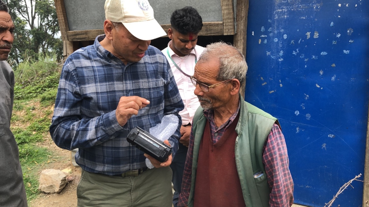 Vijay, head of Afno FM in Nepal, stands outside with an older man. Vijay is holding a radio, and talking through how to use it.