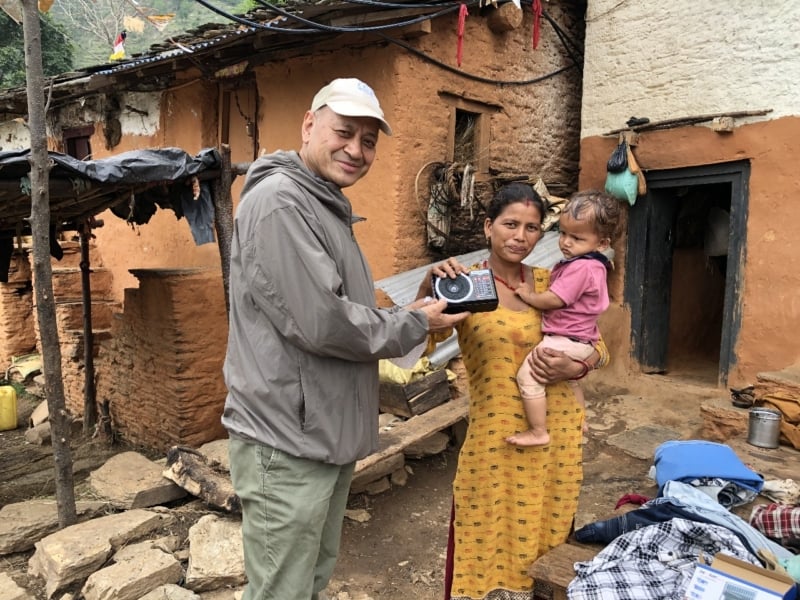 Vijay, Director of Afno FM in Nepal, hands a radio to a woman holding a small child in a rural village.