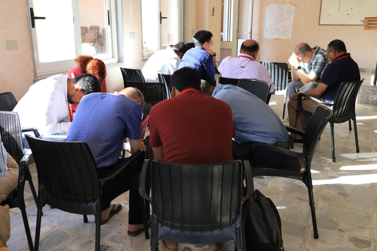 Feba partners sit together in a conference room with heads bowed in prayer.
