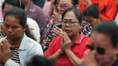 Cambodian woman in a crowd with her eyes closed and hands clasped in prayer.