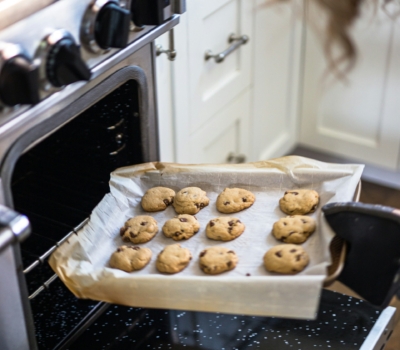 A tray of cholcolate chip cookies being taken out of an oven.