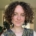 Lucy, a young woman with short brown curly hair smiling.