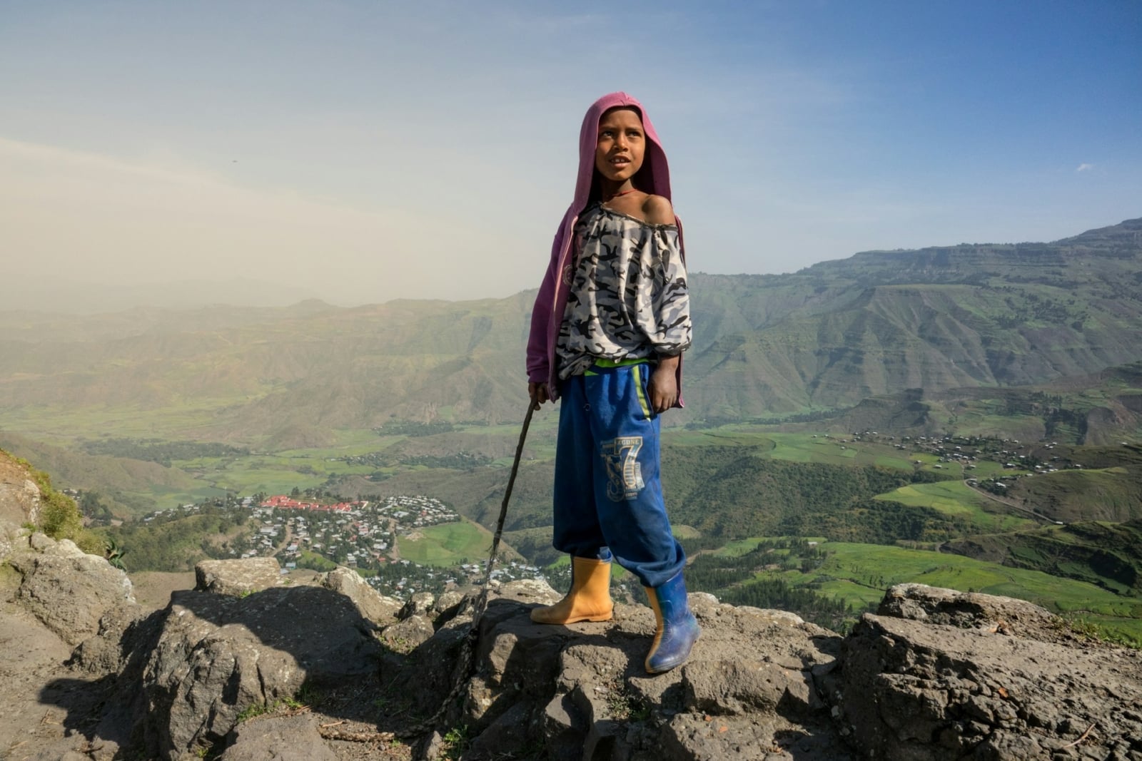 Young African boy standing on a rock with a dramatic view of mountains behind him.