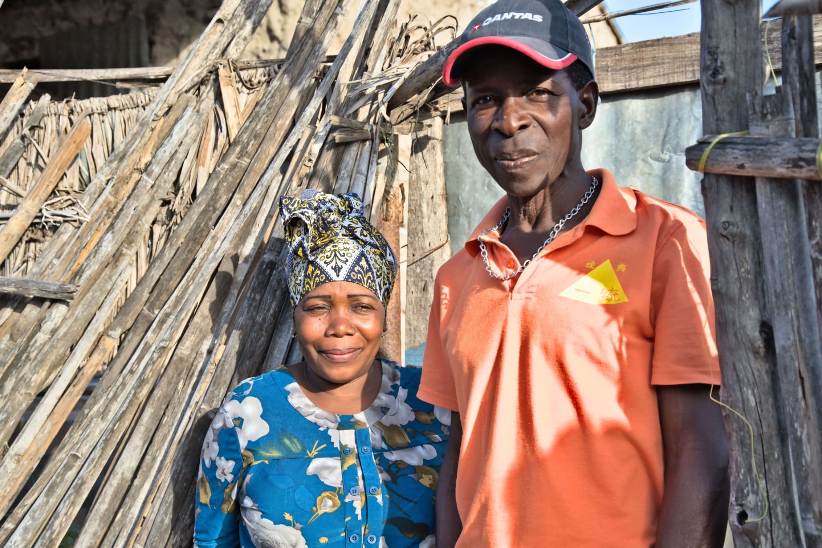A coupe stand outside a basic wooden structure in a village in Mozambique, smiling at the camera.