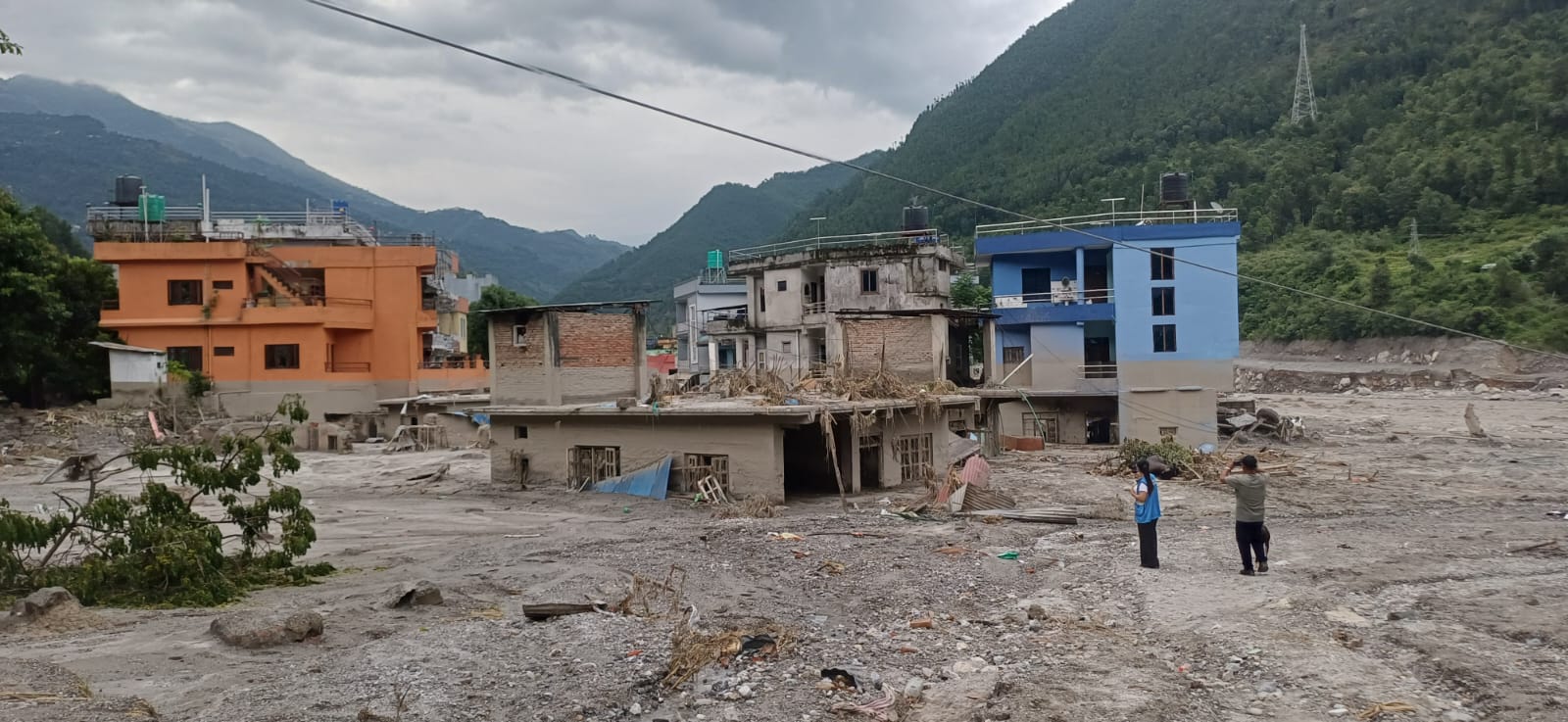 Two people look on at buildings damaged by the devastating flash flood that hit Nepal in August 2026.