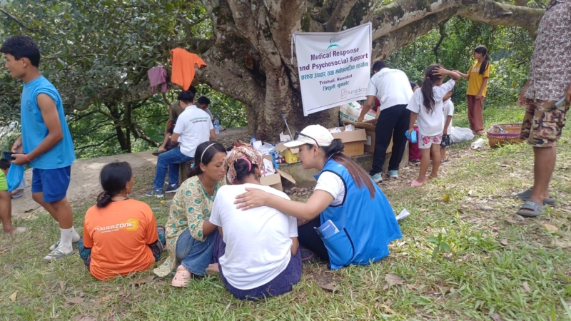 Members of the HDCS sit under a tree with people affected by the floods, offering comfort and practical support.