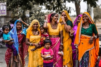 A group of Indian women and small children wearing bright saris laughing together.