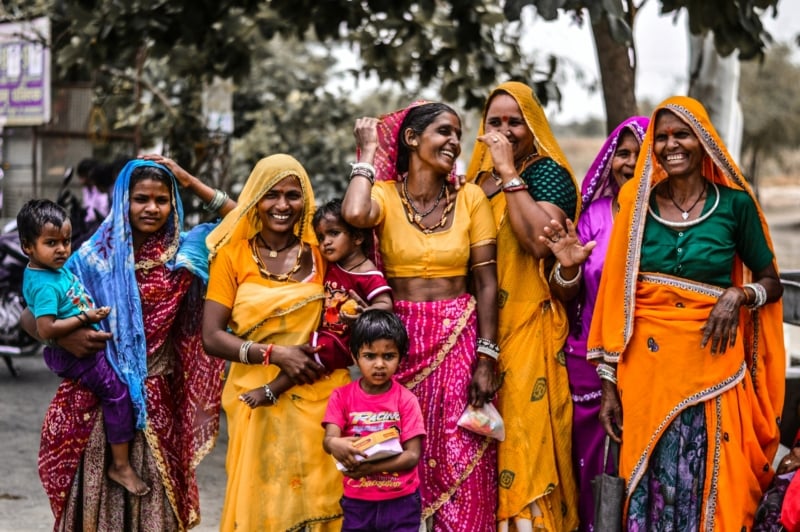 A group of Indian women and small children wearing bright saris laughing together.