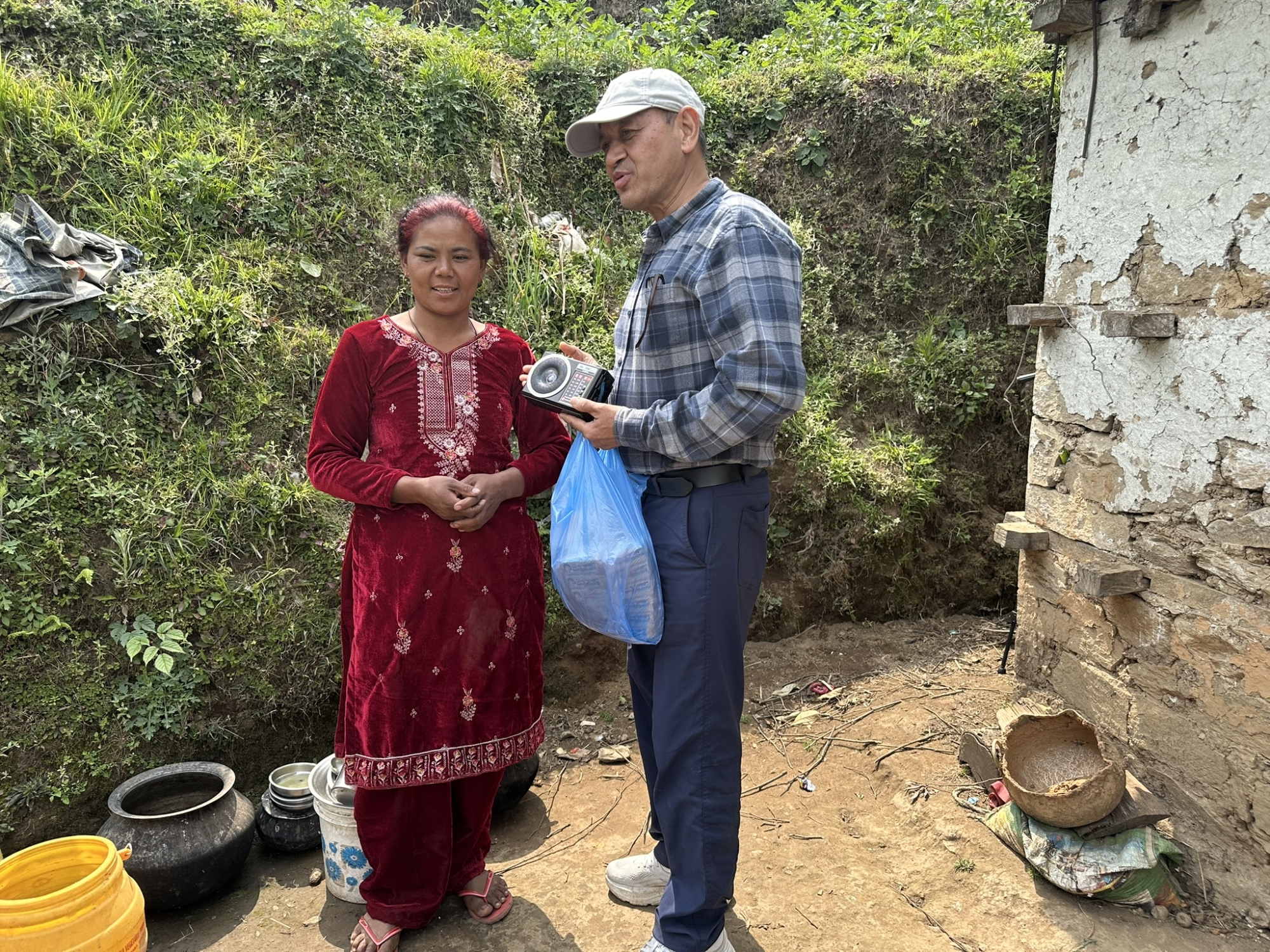 Vijay, Director of Afno FM in Nepal, handing a radio to a lady outside her house in a rural mountain village.